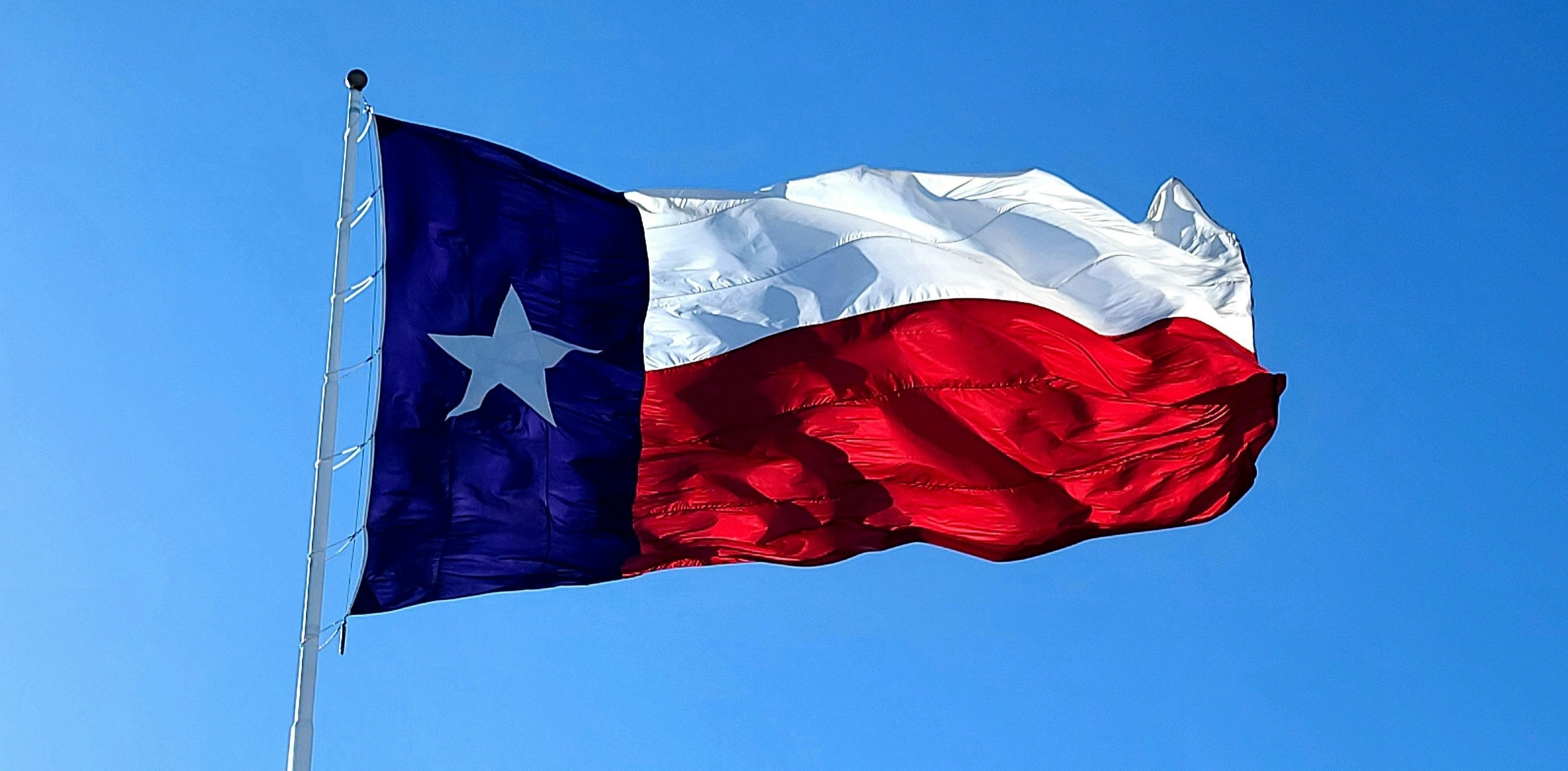 Photo by Pete Alexopoulos. The Texas flag waving against the blue sky.